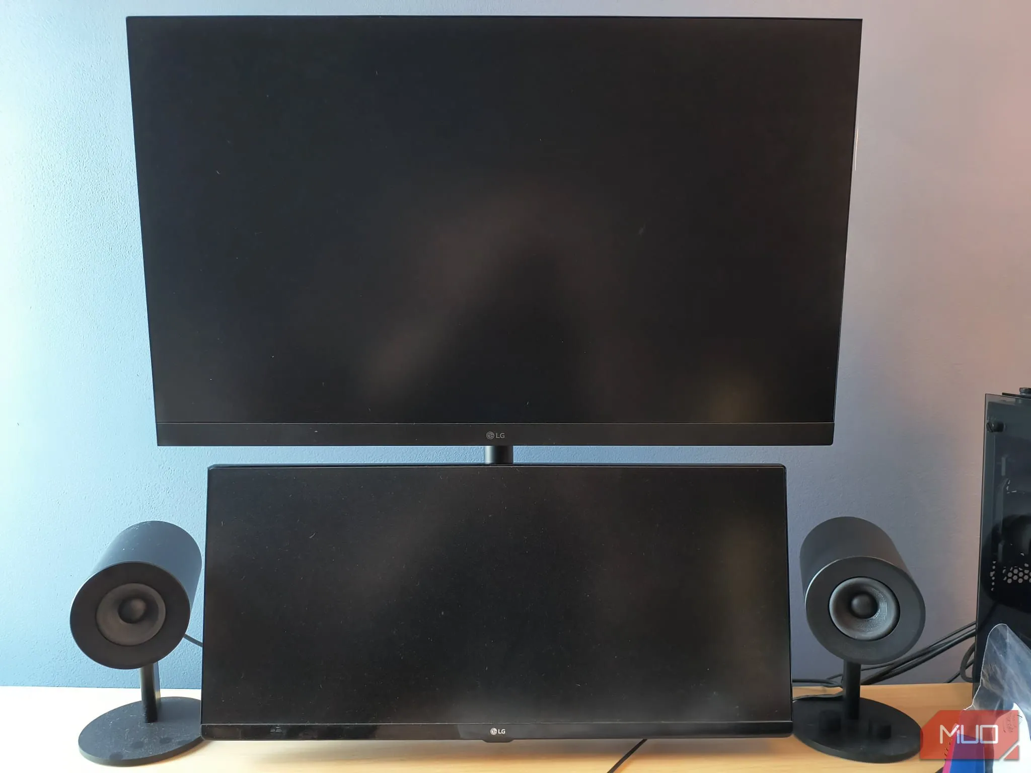 Bàn làm việc với setup hai màn hình xếp dọc sử dụng tay đỡ màn hình kép, loa đặt hai bên, tạo không gian gọn gàng và tăng năng suất.