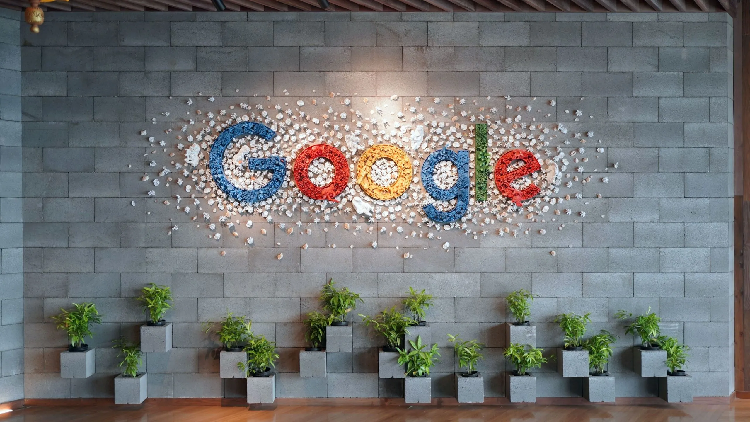 Biểu tượng Google trên bức tường văn phòng với cây xanh, thể hiện sự đồng bộ liền mạch của Chromebook với hệ sinh thái Google