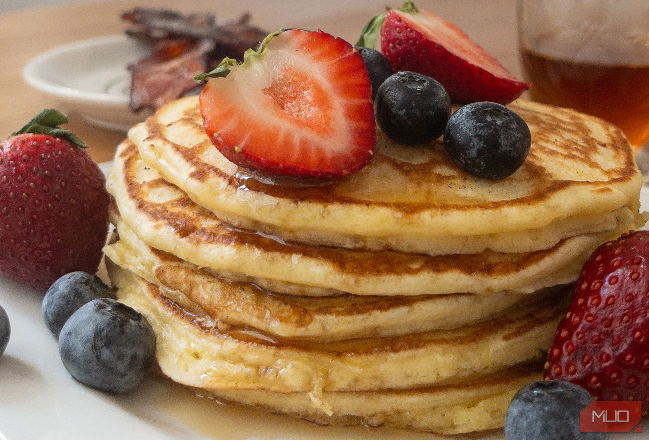 Chiếc bánh pancake mềm mịn với các loại trái cây và siro, chụp ở góc 45 độ, làm nổi bật các lớp và độ dày của món ăn.