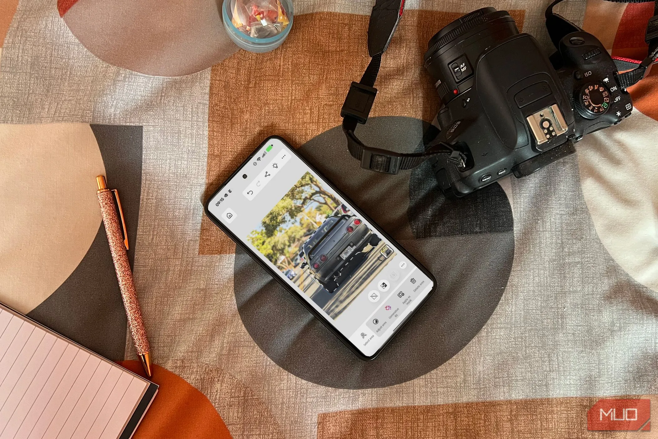 Điện thoại Android hiển thị ứng dụng Photoshop trên giường cạnh máy ảnh và sổ ghi chú