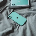 Điện thoại iPhone 11 màu xanh mint nằm trên ga trải giường, thể hiện thiết kế và chất lượng hoàn thiện bền bỉ của iPhone 11.