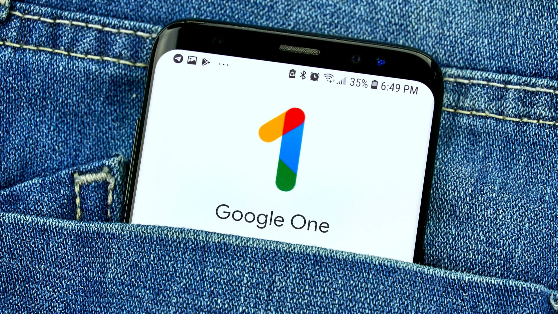 Điện thoại thông minh hiển thị ứng dụng Google One trong túi quần jean, minh họa việc sử dụng dịch vụ lưu trữ đám mây trả phí như một lớp bảo vệ cuối cùng cho ảnh.