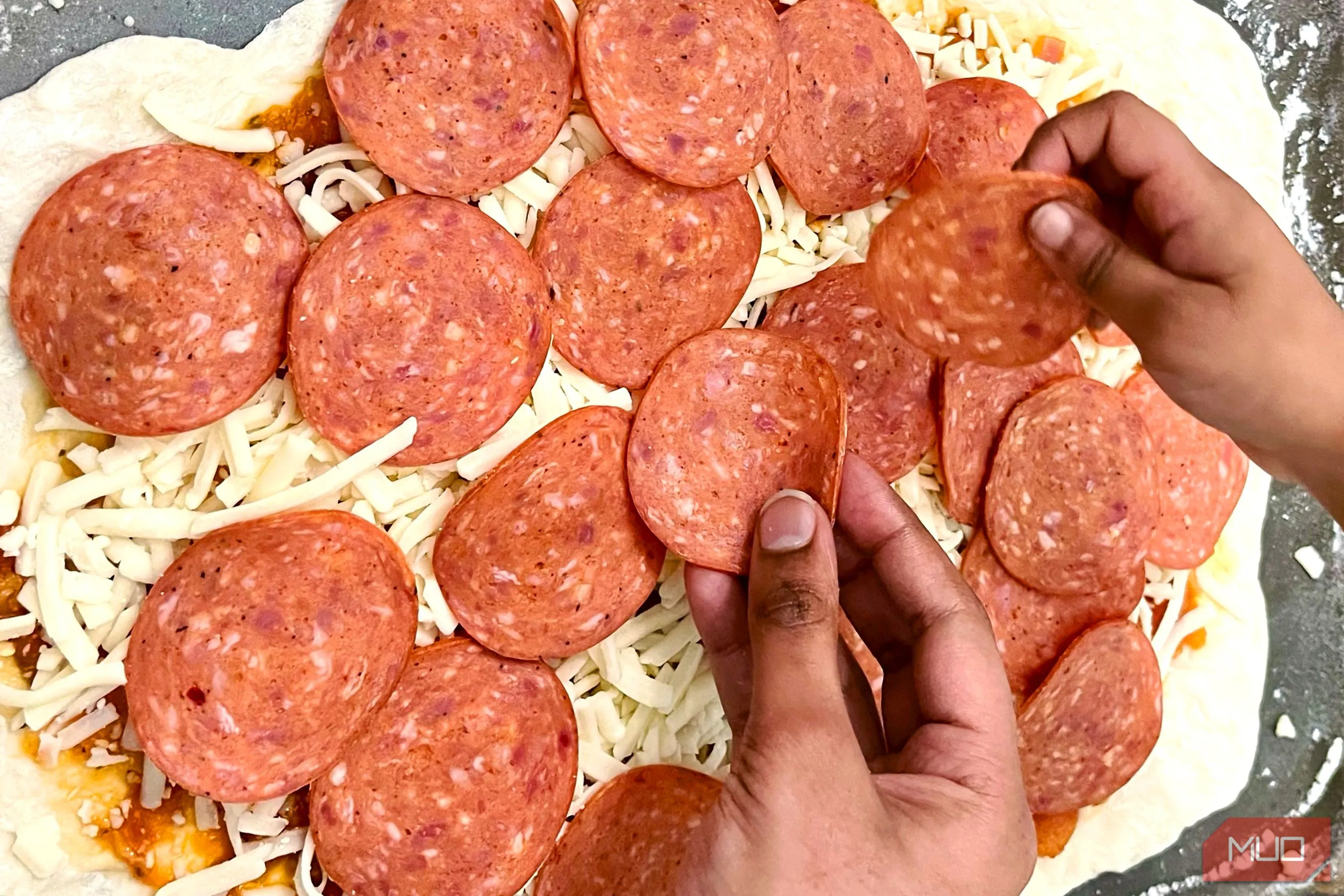 Đôi bàn tay đang rải các nguyên liệu tươi lên một chiếc pizza sắp hoàn thành, tạo cảm giác về quá trình làm ra món ăn và sự gắn kết.