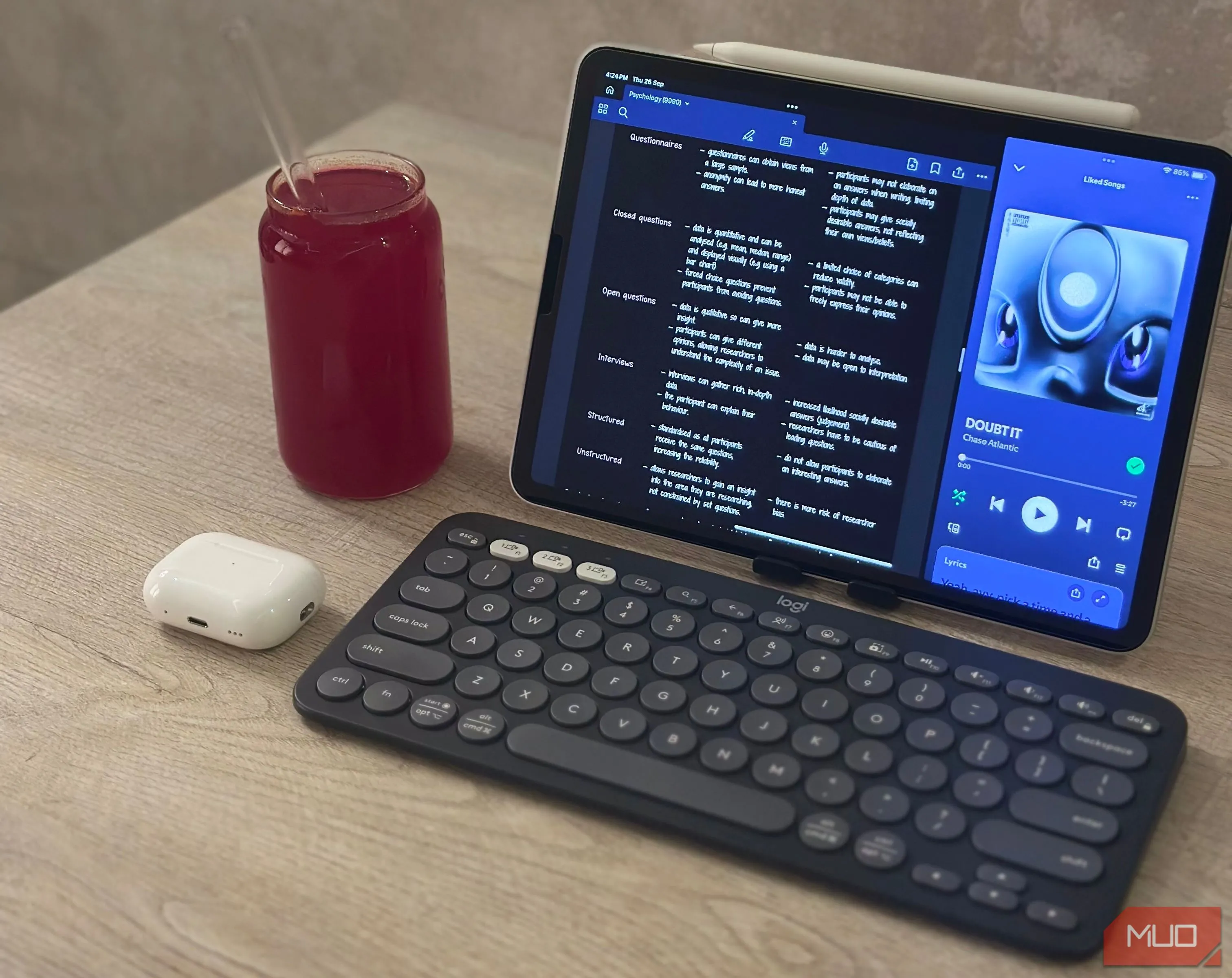 Hình ảnh iPad, bàn phím Logitech Pebble, tai nghe AirPods và cốc nước trên bàn làm việc, thể hiện setup làm việc di động với iPad