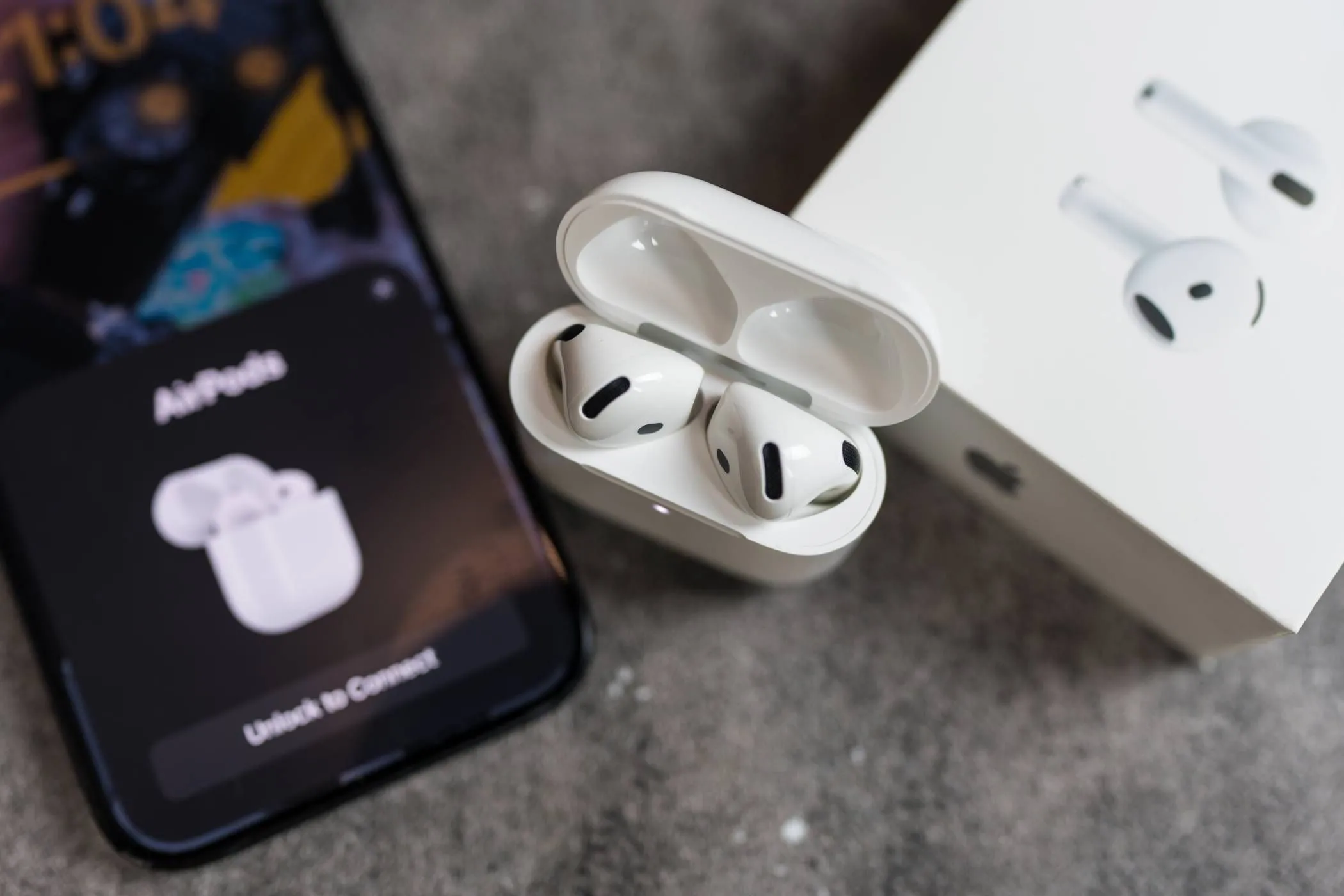 Hộp AirPods đang mở gần iPhone, màn hình iPhone hiển thị giao diện thiết lập kết nối, minh họa quá trình ghép nối nhanh chóng nhờ NFC.