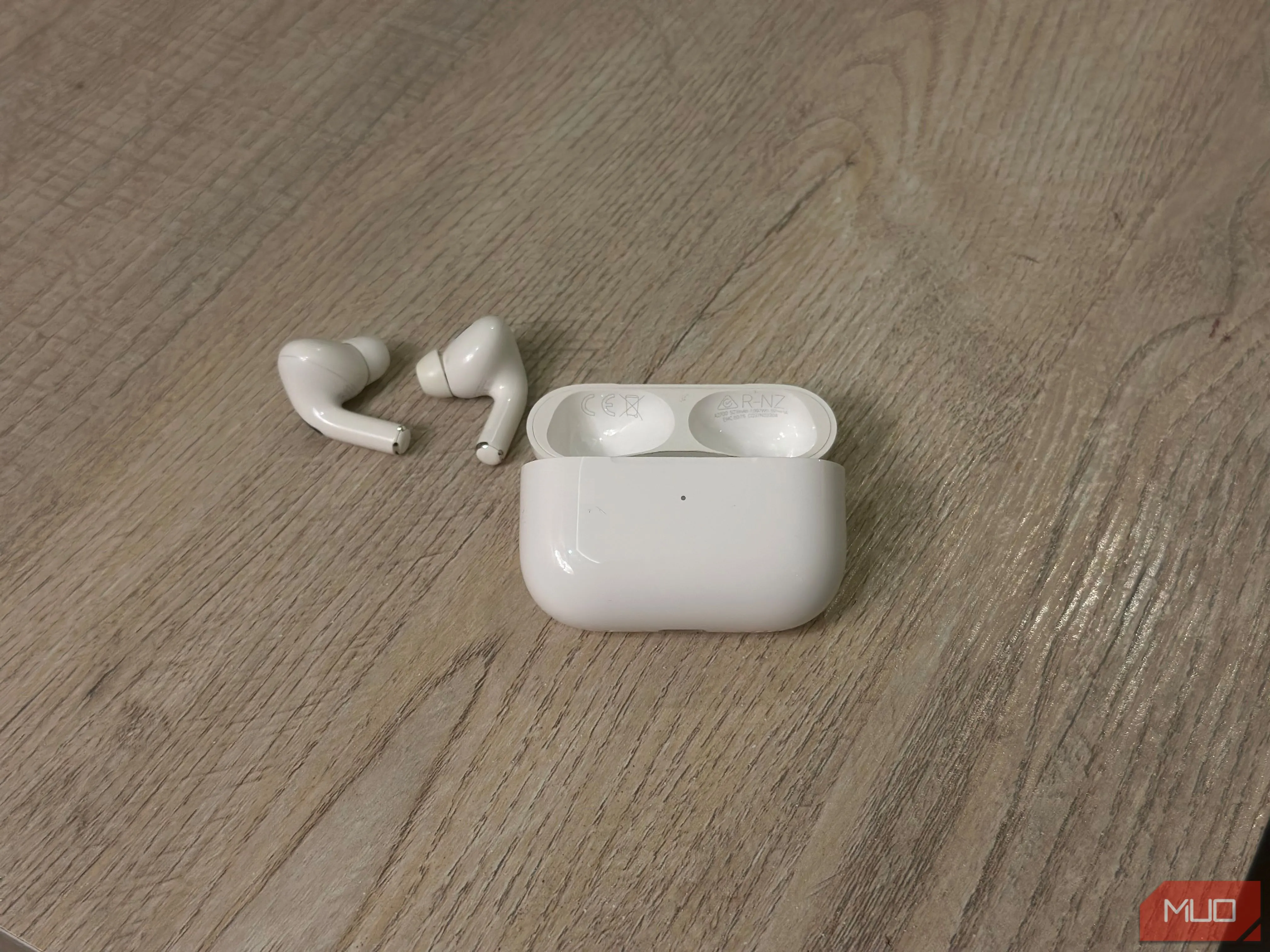 Hộp sạc AirPods đang mở và tai nghe đặt trên bàn, hiển thị vị trí số hiệu model và số sê-ri trên nắp hộp sạc.