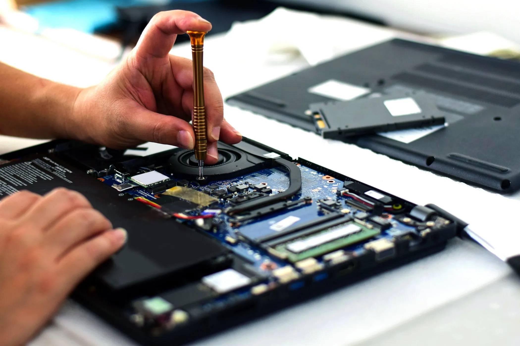 Kỹ thuật viên sử dụng tua vít sửa chữa bo mạch chủ laptop, tượng trưng cho việc bảo trì và định dạng ổ cứng nhanh chóng.