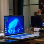 Laptop Windows màu bạc trên bàn kính, minh họa giao diện màn hình chính