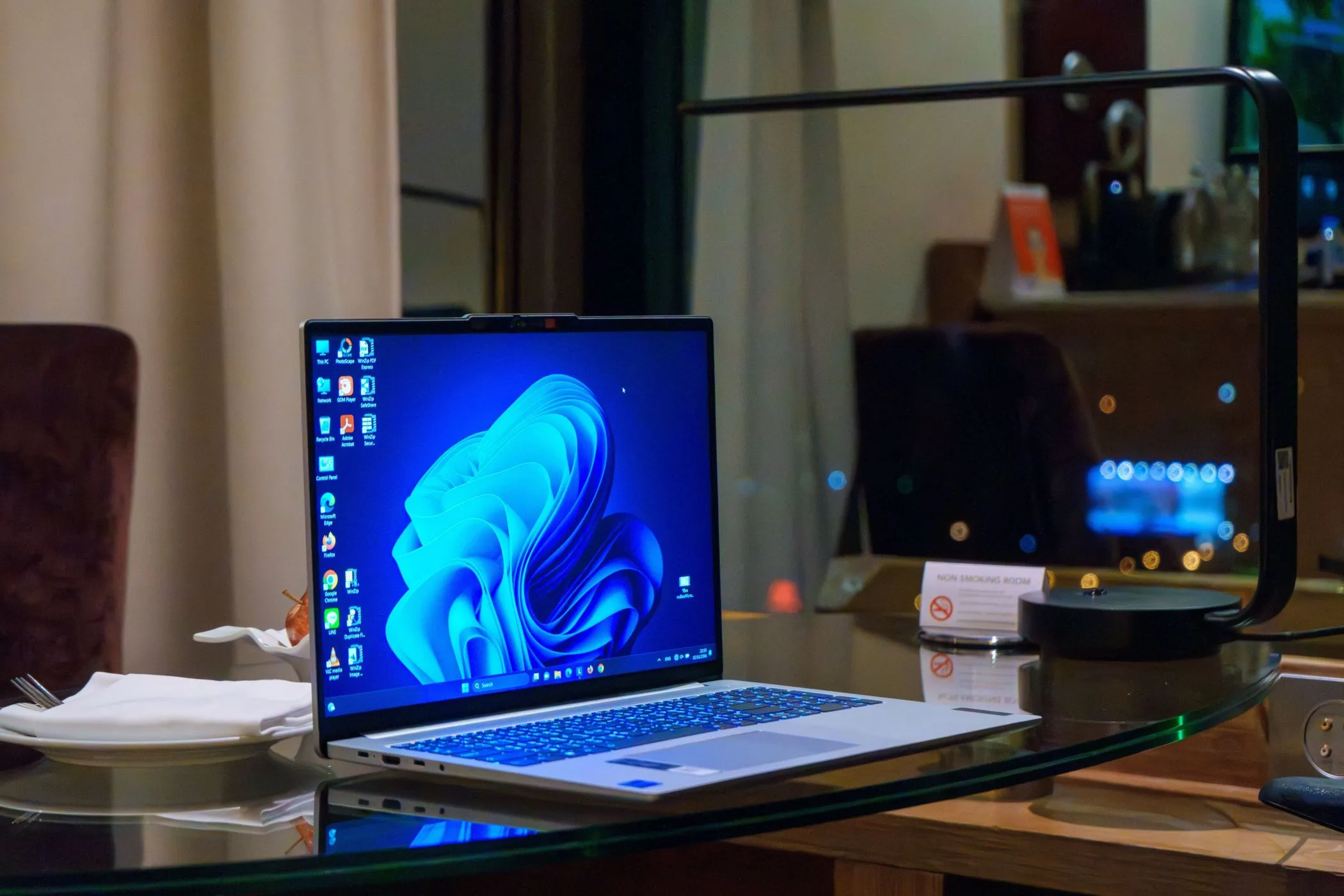Laptop Windows màu bạc trên bàn kính, minh họa giao diện màn hình chính