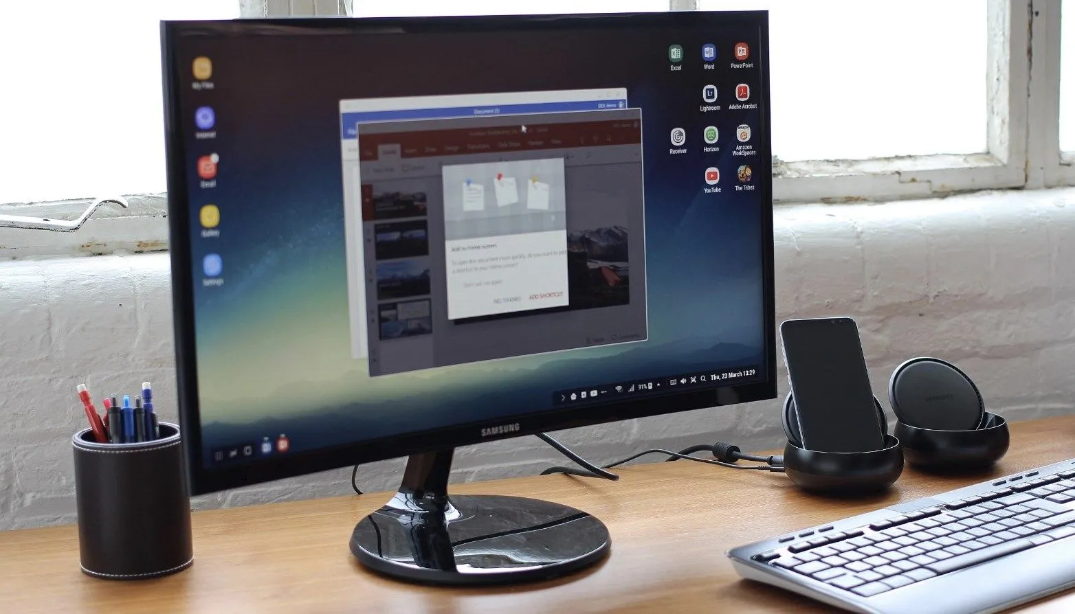 Màn hình Samsung hiển thị giao diện DeX, kết nối với bàn phím và hệ thống âm thanh, tạo không gian làm việc như máy tính.