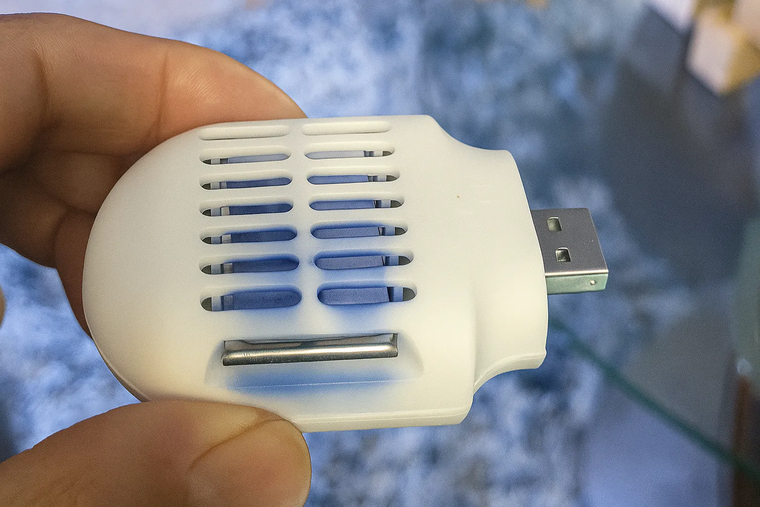 Một bàn tay đang cầm một thiết bị đuổi muỗi nhỏ gọn, màu trắng, chạy bằng USB.