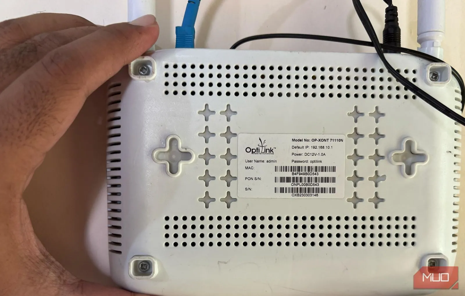 Một bàn tay đang cầm router và chỉ vào mặt sau, nơi thường in thông tin đăng nhập mặc định