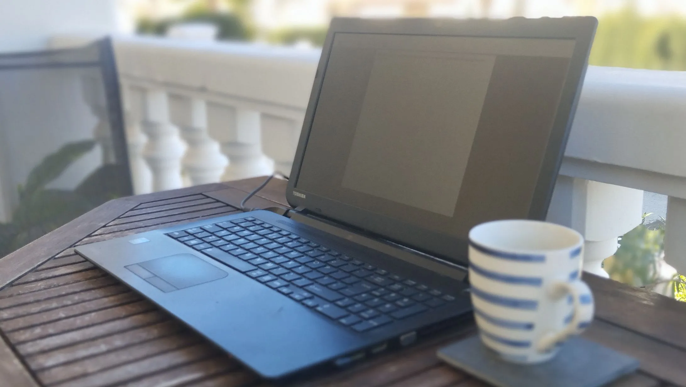 Một chiếc laptop Toshiba được tái sử dụng đặt trên bàn cùng với tách cà phê, biểu tượng cho một môi trường làm việc tập trung và hiệu quả