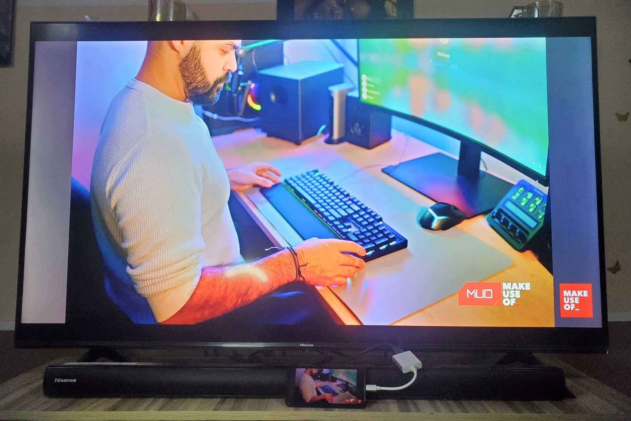 Một chiếc smartphone được kết nối với TV qua bộ chuyển đổi USB-C sang HDMI, phản chiếu màn hình và hiển thị một người đàn ông đang sử dụng bàn phím