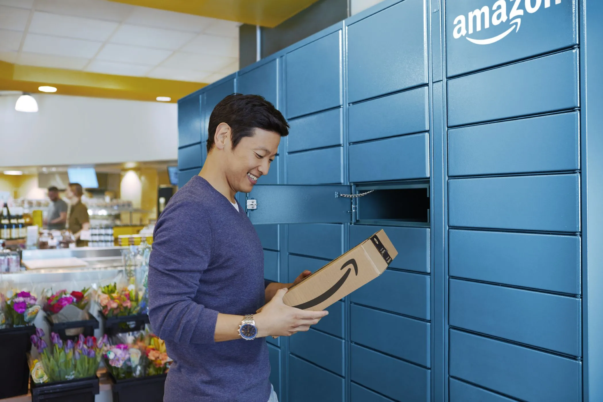 Một người đàn ông đang lấy gói hàng từ tủ khóa Amazon Locker, minh họa cách nhận hàng tiện lợi và bảo mật địa chỉ nhà riêng khi mua sắm online.