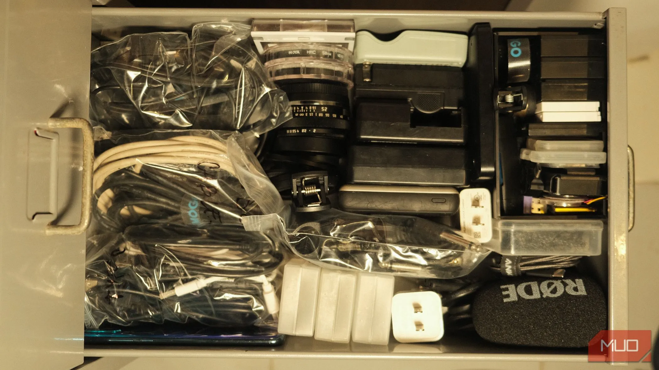 Ngăn kéo chứa thiết bị và phụ kiện công nghệ đã được sắp xếp gọn gàng theo mức độ sử dụng và hình dạng, với các túi zip đựng cáp được dán nhãn.