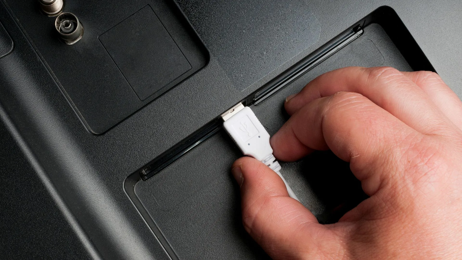 Người đàn ông cắm cáp USB Type-A vào cổng phía sau TV, minh họa việc sử dụng sai loại cáp sạc USB cho thiết bị điện tử.