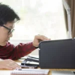 Người đàn ông kiểm tra máy in trên bàn làm việc, thể hiện sự bối rối khi gặp lỗi in ấn.