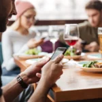 Người đàn ông sử dụng điện thoại trong quán cà phê cùng bạn bè