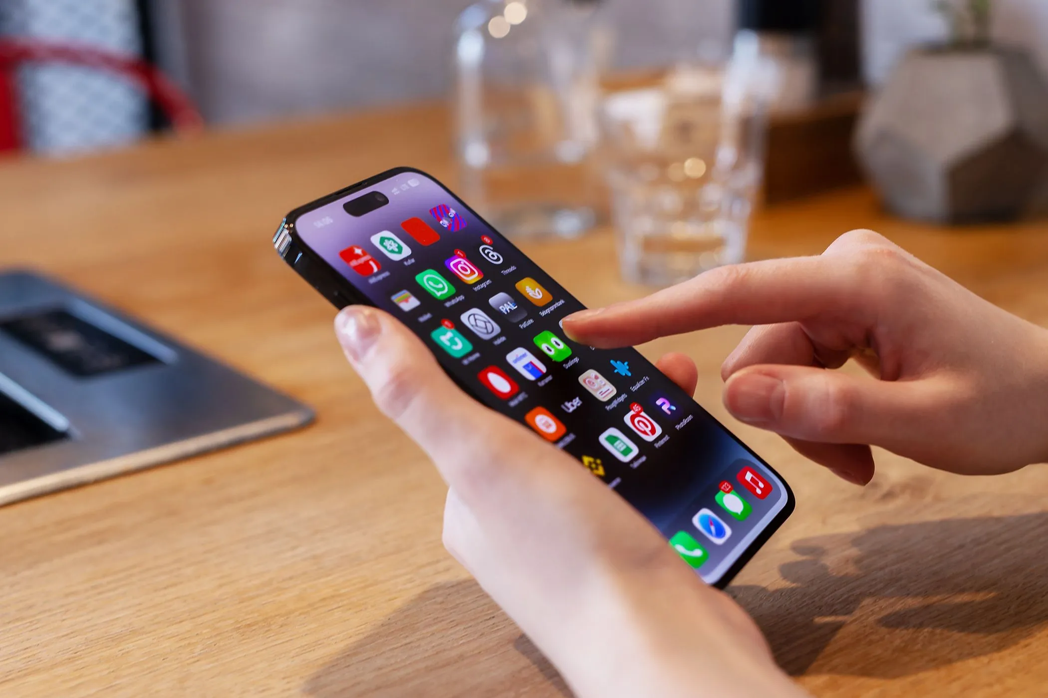 Người dùng đang sử dụng iPhone trên bàn với cốc nước phía sau, tượng trưng cho trải nghiệm cá nhân