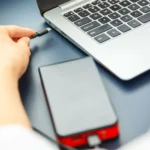 Người phụ nữ cắm cáp USB-C vào laptop và sạc dự phòng, minh họa việc chia sẻ nguồn điện khi sạc laptop