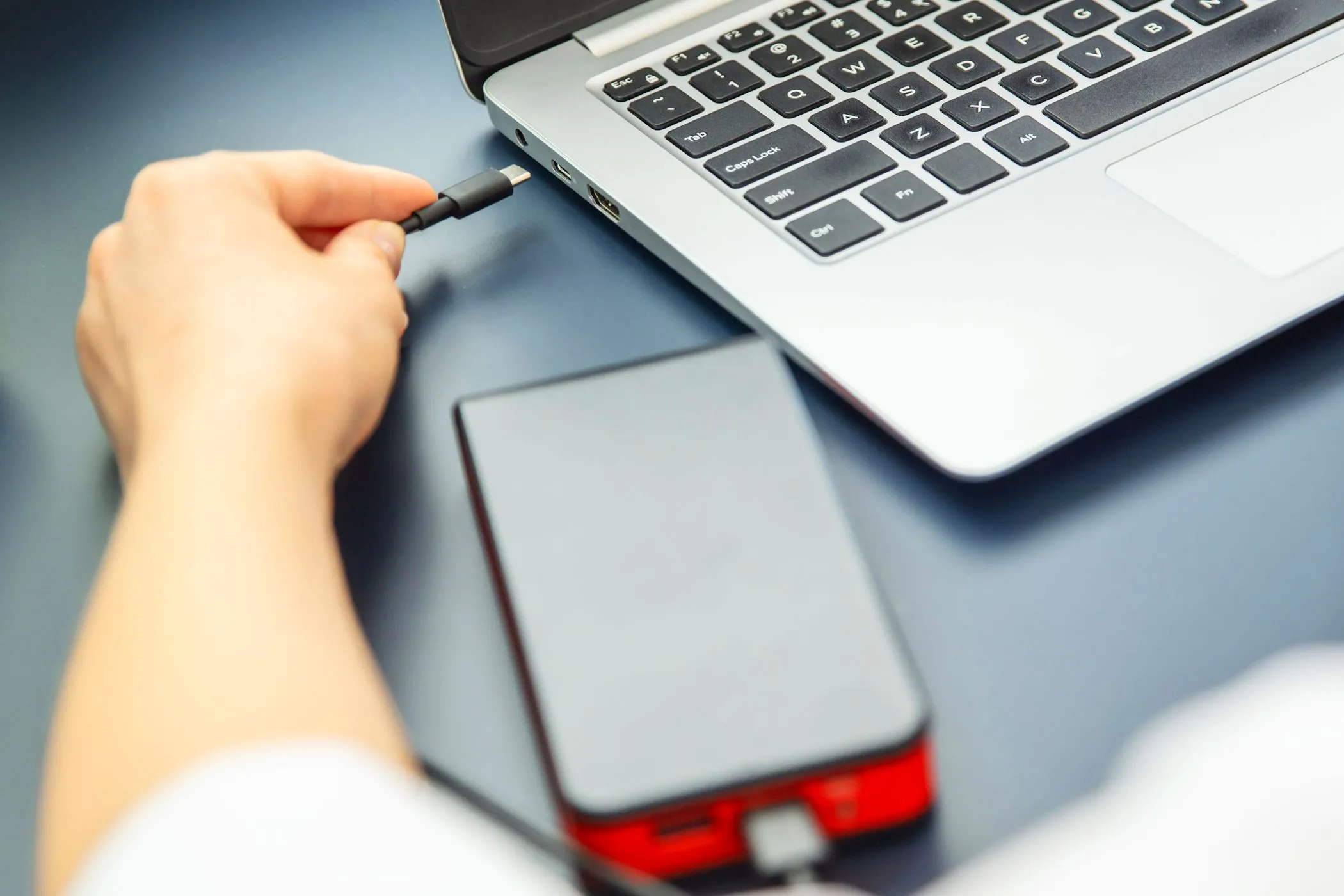Người phụ nữ cắm cáp USB-C vào laptop và sạc dự phòng, minh họa việc chia sẻ nguồn điện khi sạc laptop