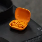 Powerbeats Pro 2 màu cam, với thiết kế móc tai đặc trưng, nằm trên một bề mặt phẳng.