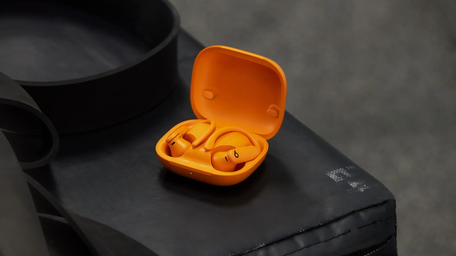 Powerbeats Pro 2 màu cam, với thiết kế móc tai đặc trưng, nằm trên một bề mặt phẳng.