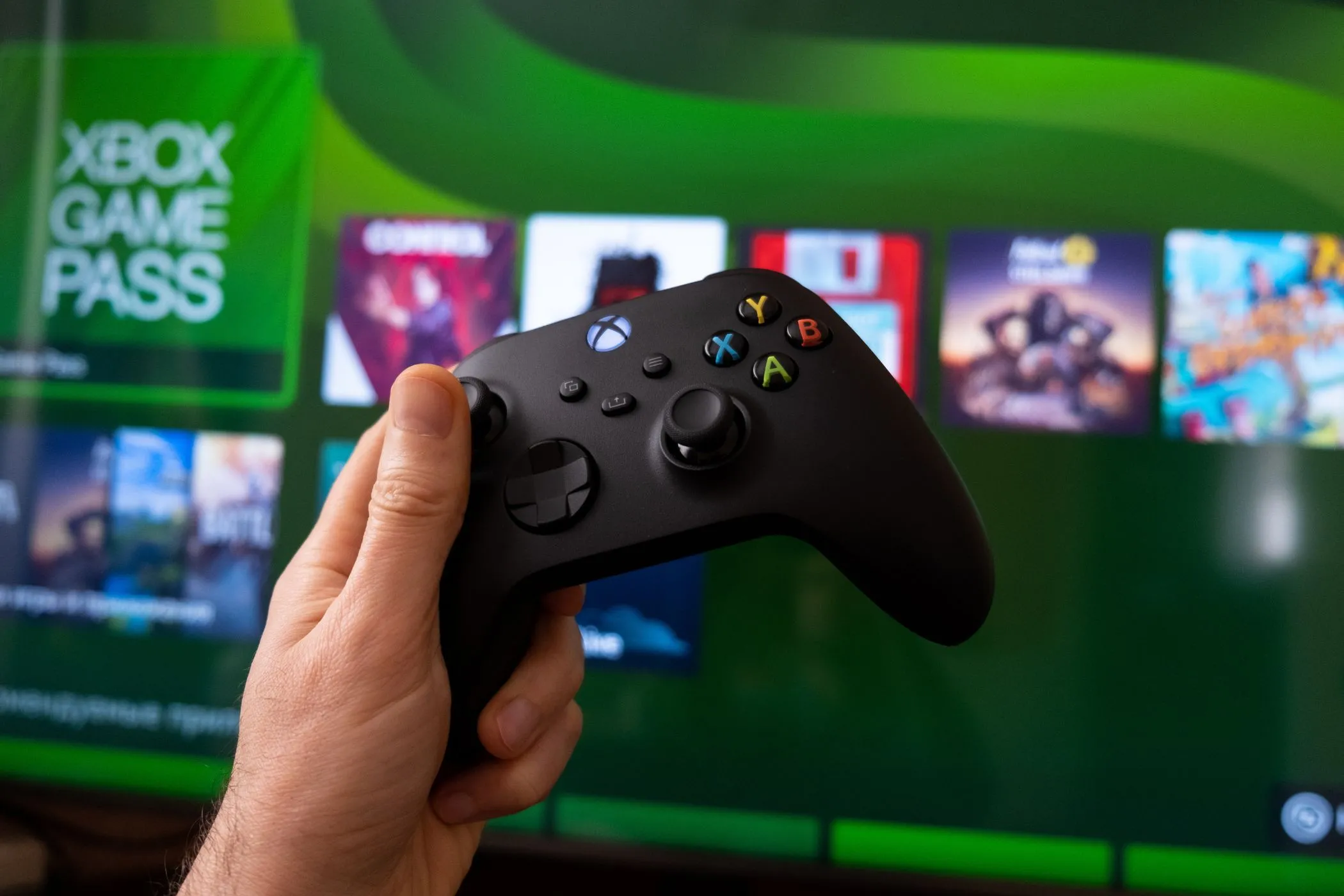 Tay cầm Xbox Controller màu đen và màn hình hiển thị Xbox Game Pass, minh họa trải nghiệm chơi game trên TV và soundbar.